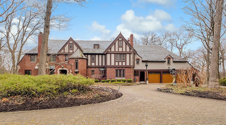 This Tudor-style home features almost 7,000 sq. ft. of living space with 6 bedrooms and a walk-out lower level. A circular brick driveway winds through woods on the 5.6-acre lot to the 3-car garage with wood doors. CONTRIBUTED PHOTO
