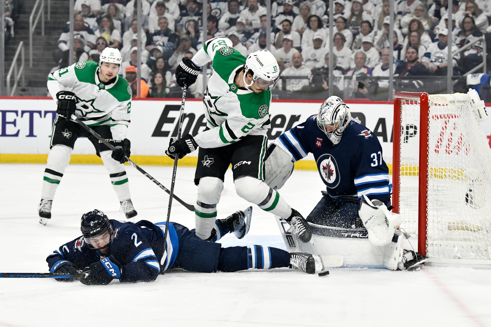 Winnipeg Jets goaltender Connor Hellebuyck (37) makes a save on Dallas Stars' Mason Marchment (27) as Dylan Demelo (2) defends during first period NHL playoff hockey action in Winnipeg, Thursday, May 15, 2025. (Fred Greenslade/The Canadian Press via AP)