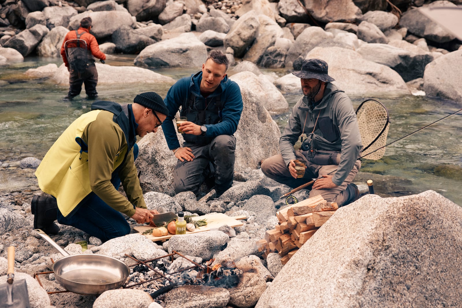 This image released by National Geographic shows Stanley Tucci, left, preparing a dish for anglers on the banks of the Sarca River during a visit to Italy's northernmost region, during the filming of his series "Tucci in Italy." (Matt Holyoak/National Geographic via AP)