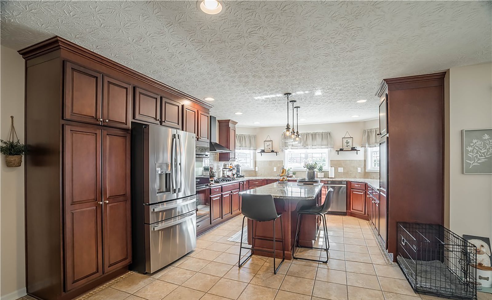 The kitchen has tile flooring, wood cabinets, an island with seating and stainless appliances, including a gas cooktop and wall ovens. CONTRIBUTED