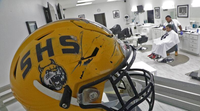 A Springfield Wildcats' football helmet sits on a shelf with other memorabilia in the Champion City Cuts barbershop as Dwain Garrett cuts Aaron Harris' hair Wednesday. BILL LACKEY/STAFF