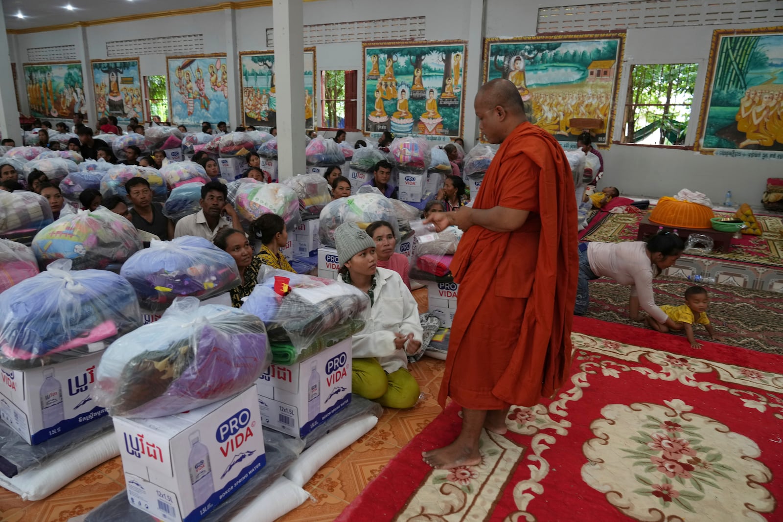 A Cambodian Buddhist monk greets villagers who wait to receive supplies donated by a charity for refugees, in Srey Snam district, Siem Reap province, Cambodia, Monday, July 28, 2025, amid the fighting between Thailand and Cambodia. (AP Photo/Heng Sinith)