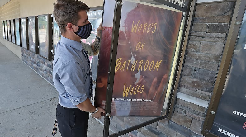 Noah Canter, assistant manager at the UEC Cinema 10 in Springfield, puts a "Now Showing" movie poster up outside the theater Friday on the first day they've been open in five months. BILL LACKEY/STAFF