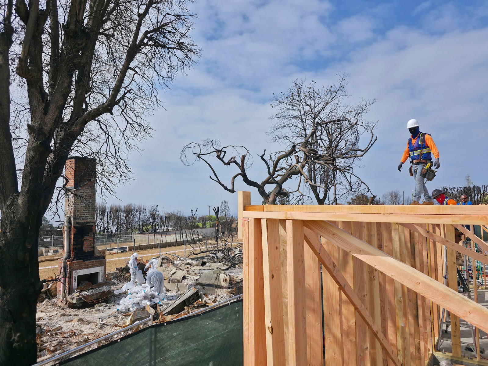 A worker stands atop a home being rebuilt after the Palisades Fire in the Pacific Palisades neighborhood of Los Angeles, Thursday, April 24, 2025. (AP Photo/Damian Dovarganes)