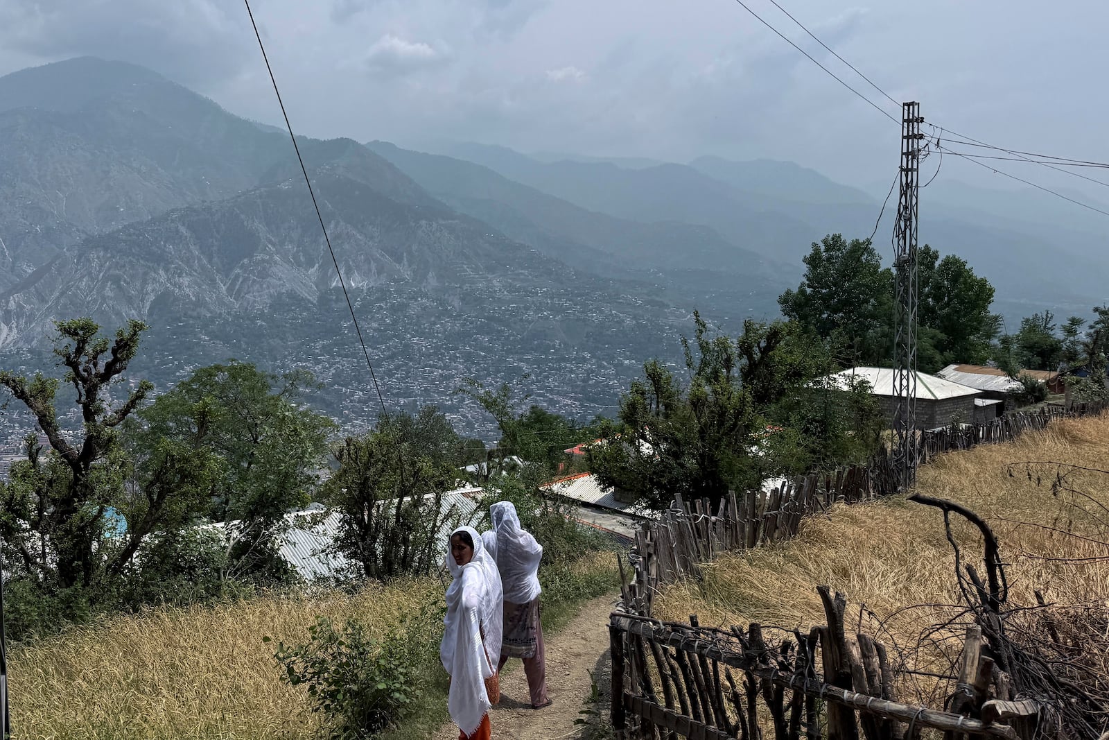 Villager women walk on a dusty track during a government's organized trip for media to Bella Noor Shah, a mountainous village near Muzaffarabad, the capital of Pakistan administered Kashmir, Monday, May 5, 2025. (AP Photo/Muhammad Yousuf, Pool)