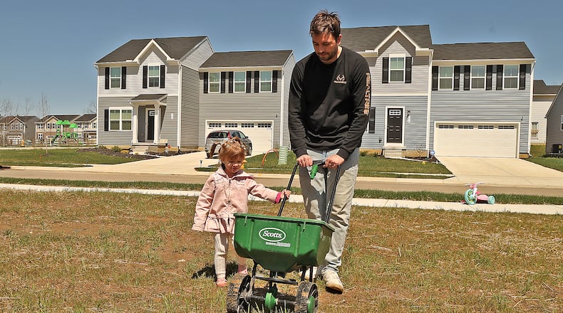 Riley Goss, 2, helps her father, Nick, sew grass seed in their new yard in the Bridgewater development Thursday. BILL LACKEY/STAFF