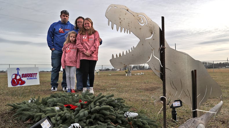 Barrett Fitzsimmons' parents Brad and Lana along with his sisters Brayden and Braelynn look over Barrett's grave at Myers Cemetery in Pike Township Thursday. Two years after Barrett died at the age of 9-years-old from cancer the family is still not permitted to place a permanent headstone on his grave because of a disagreement with the cemetery trustees over the design. A metal cutout of a dinosaur, which Barrett loved, is the only thing that marks the grave. BILL LACKEY/STAFF