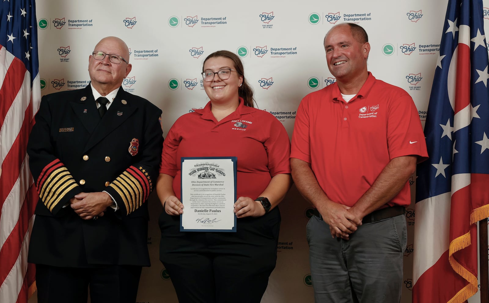 Danielle Paulus, center, holds a certificate as he stands next to State Fire Marshal Kevin Reardon, left, and Mitch Blackford, Ohio Department of Transportation (ODOT) assistant director of field operations, during an event honoring ODOT employees who serve as volunteer firefighters or EMTs on Tuesday, Aug. 19, 2025, at Clark State College. JOSEPH COOKE/STAFF