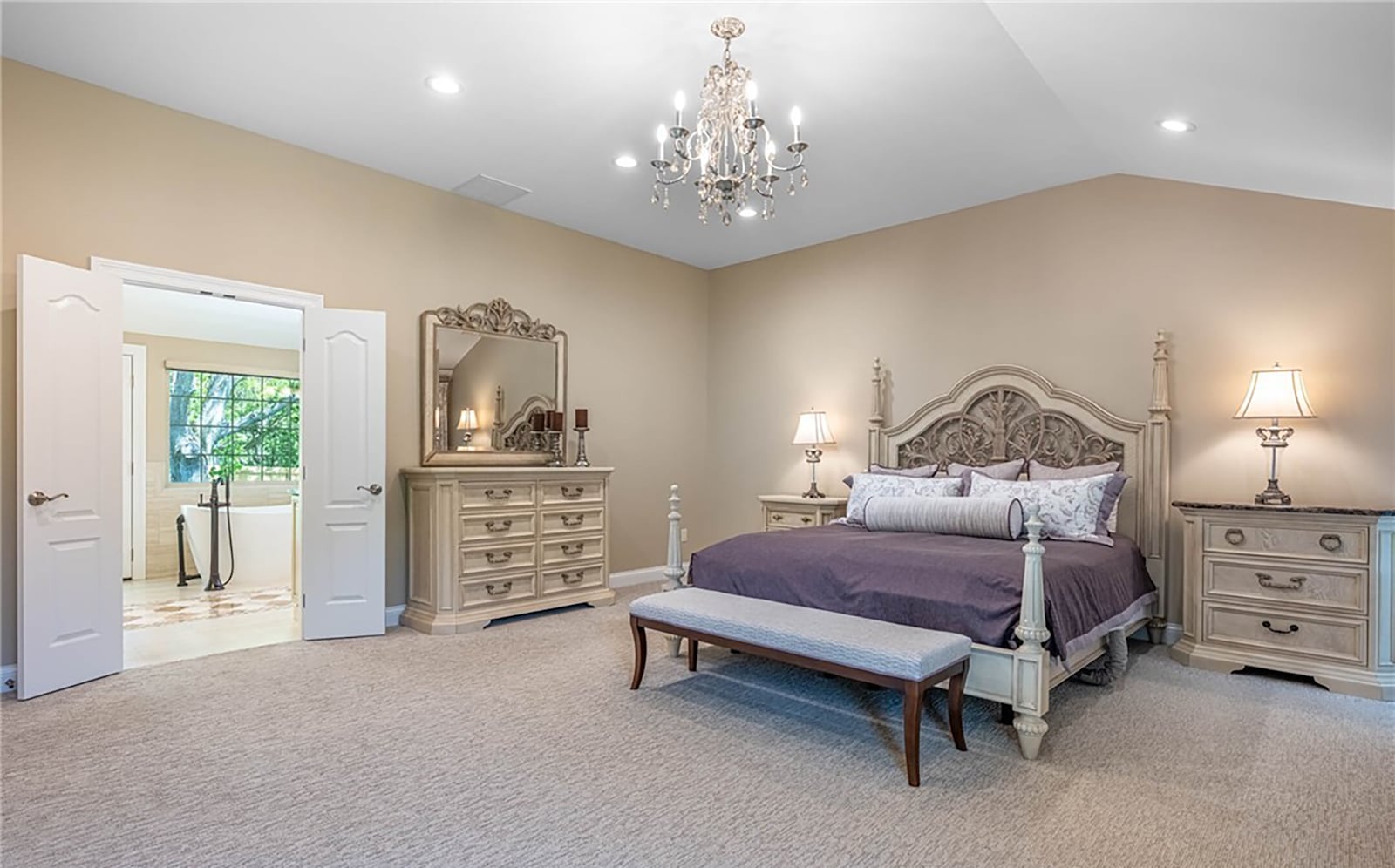The primary bedroom suite has carpeting and a decorative chandelier. It also has a vaulted ceiling and recessed lighting.