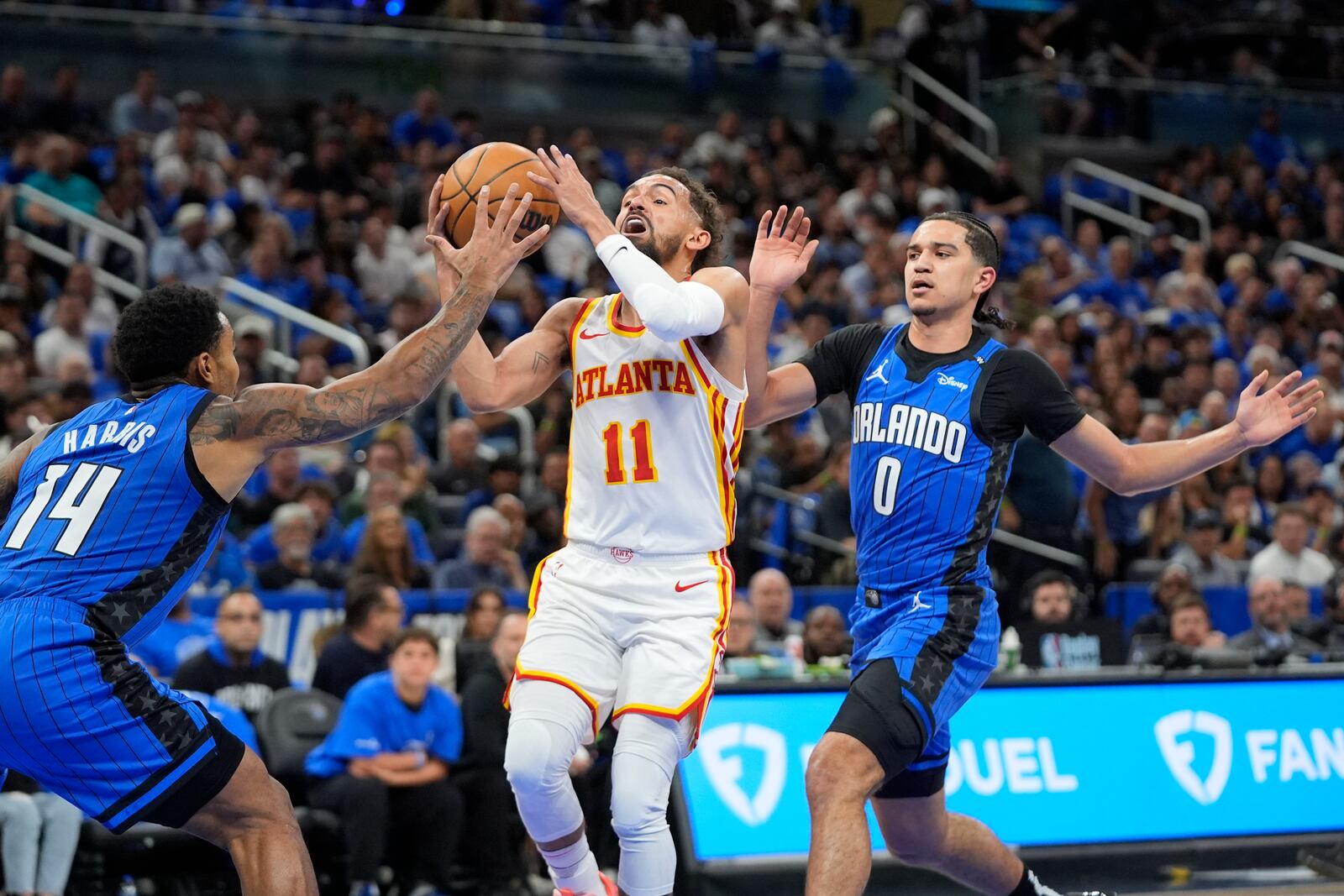 Atlanta Hawks guard Trae Young (11) attempts a shot as he goes between Orlando Magic guard Gary Harris (14) and guard Anthony Black (0) during the first half of an NBA play-in tournament basketball game, Tuesday, April 15, 2025, in Orlando, Fla. (AP Photo/John Raoux)