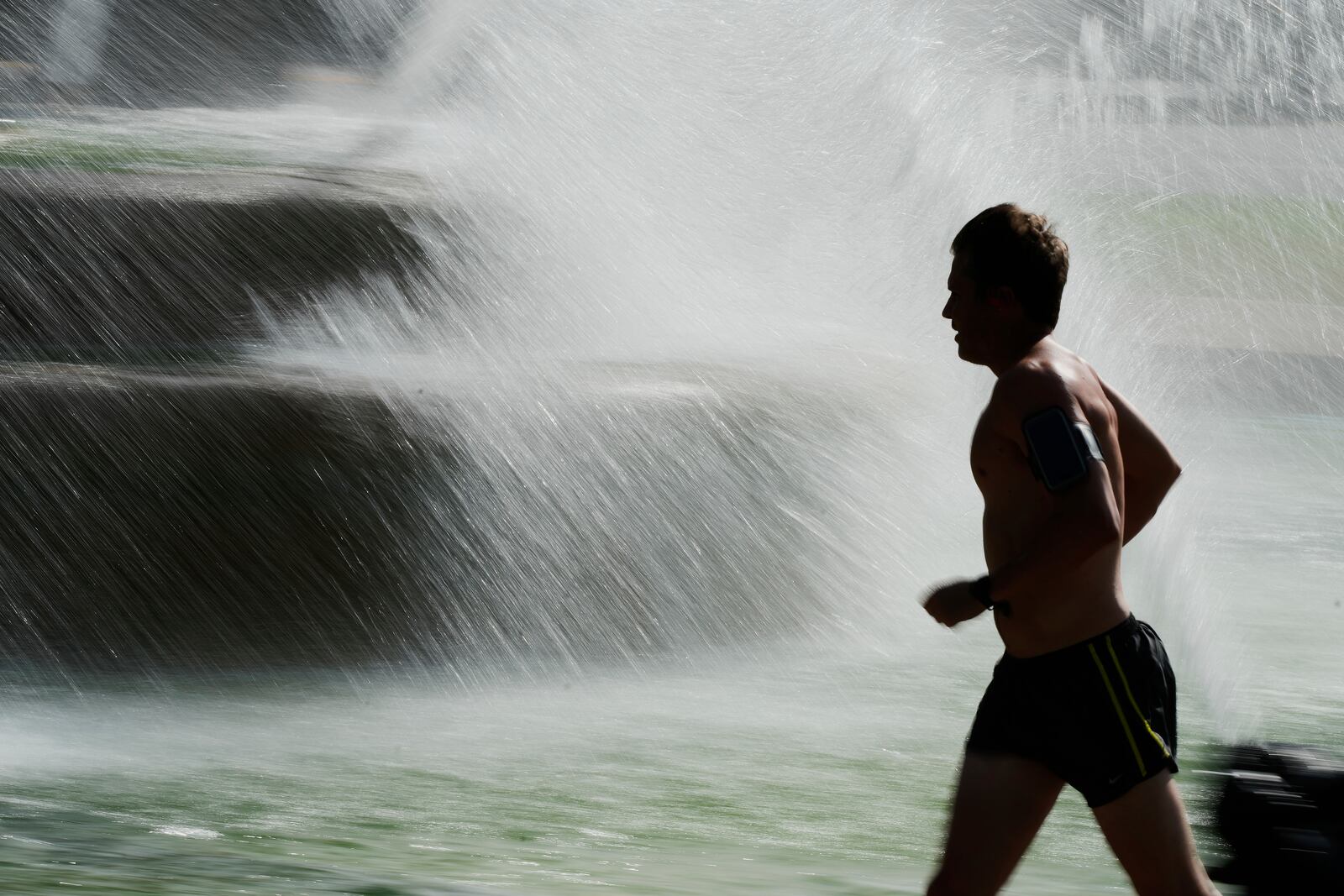 A man runs past a fountain as temperatures approach 100 degrees, Friday, June 20, 2025, in Kansas City, Mo. (AP Photo/Charlie Riedel)