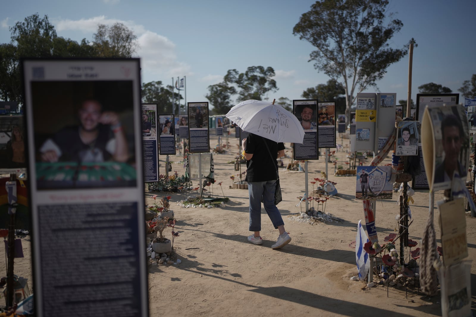A woman walks with an umbrella reading 'End the war immediately,' during a protest demanding immediate release of hostages held by Hamas in the Gaza Strip, at the site of the October 7, 2023, Hamas attack on the Nova music festival near Kibbutz Re'im in southern Israel, Wednesday, July 2, 2025. (AP Photo/Ohad Zwigenberg)