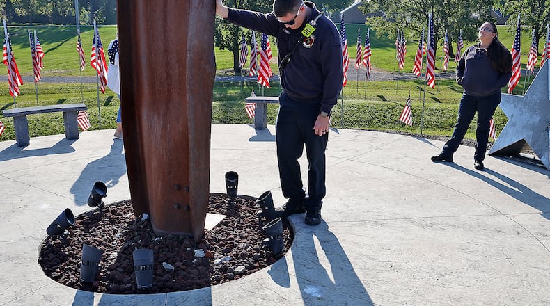 Mechanicsburg Firefighter Zach Sprinkle touches the World Trade Center artifact as he takes a moment while visiting Freedom Grove in Urbana for the 9/11 Memorial Service Monday, Sept. 11, 2023. BILL LACKEY/STAFF