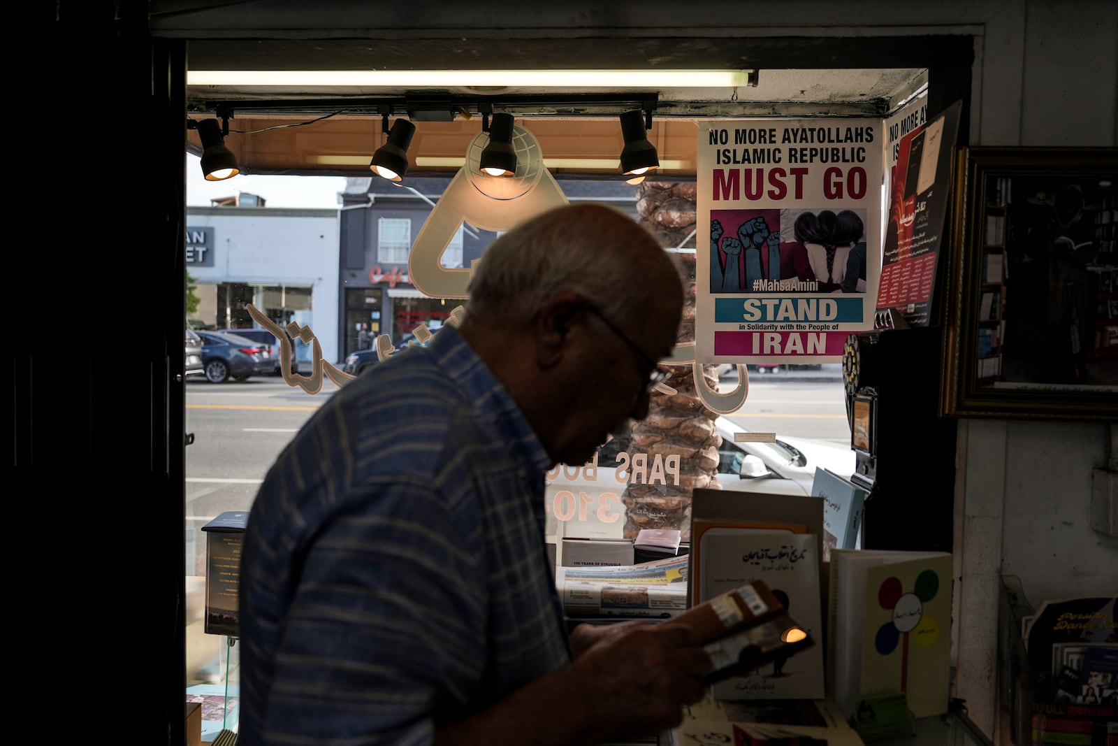 Sam Beykzadeh works in his bookstore in the "Tehrangeles" neighborhood of Los Angeles Tuesday, June 24, 2025, as a poster in the window calls for regime change in Iran. (AP Photo/Jae C. Hong)