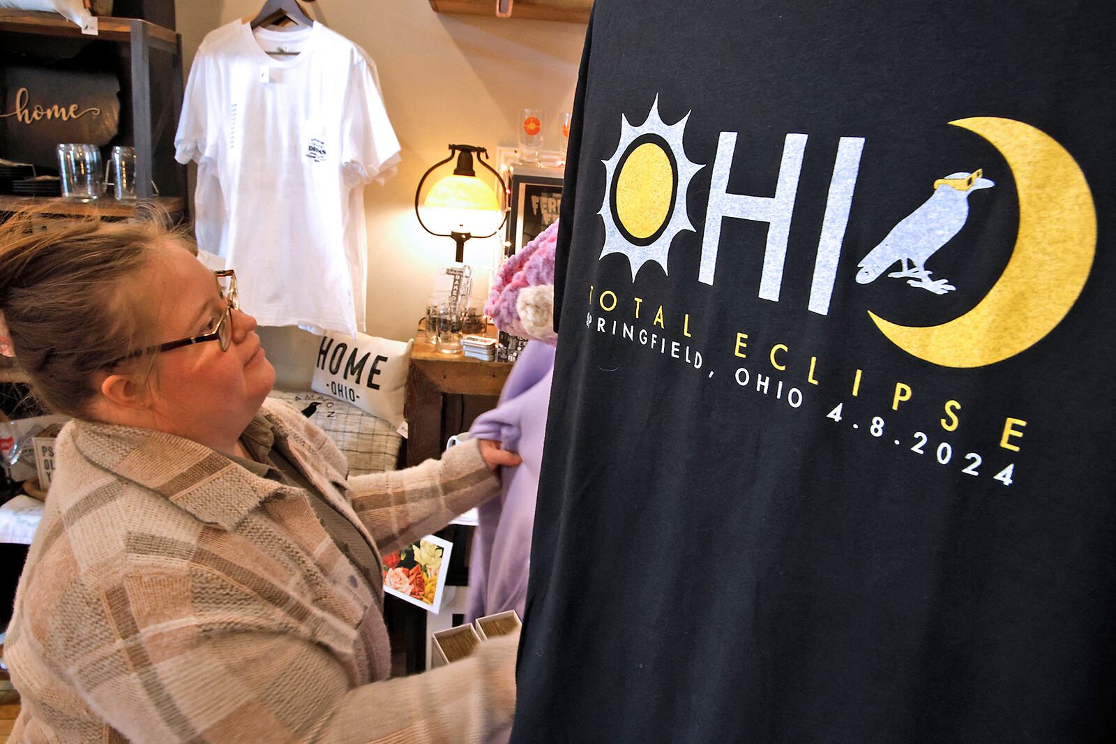 Jordan Lyons straightens a display at Champion City Guide and Supply Wednesday, March 20, 2024. The new total eclipse t-shirts, on sale at the downtown Springfield store, have quickly become very popular. BILL LACKEY/STAFF