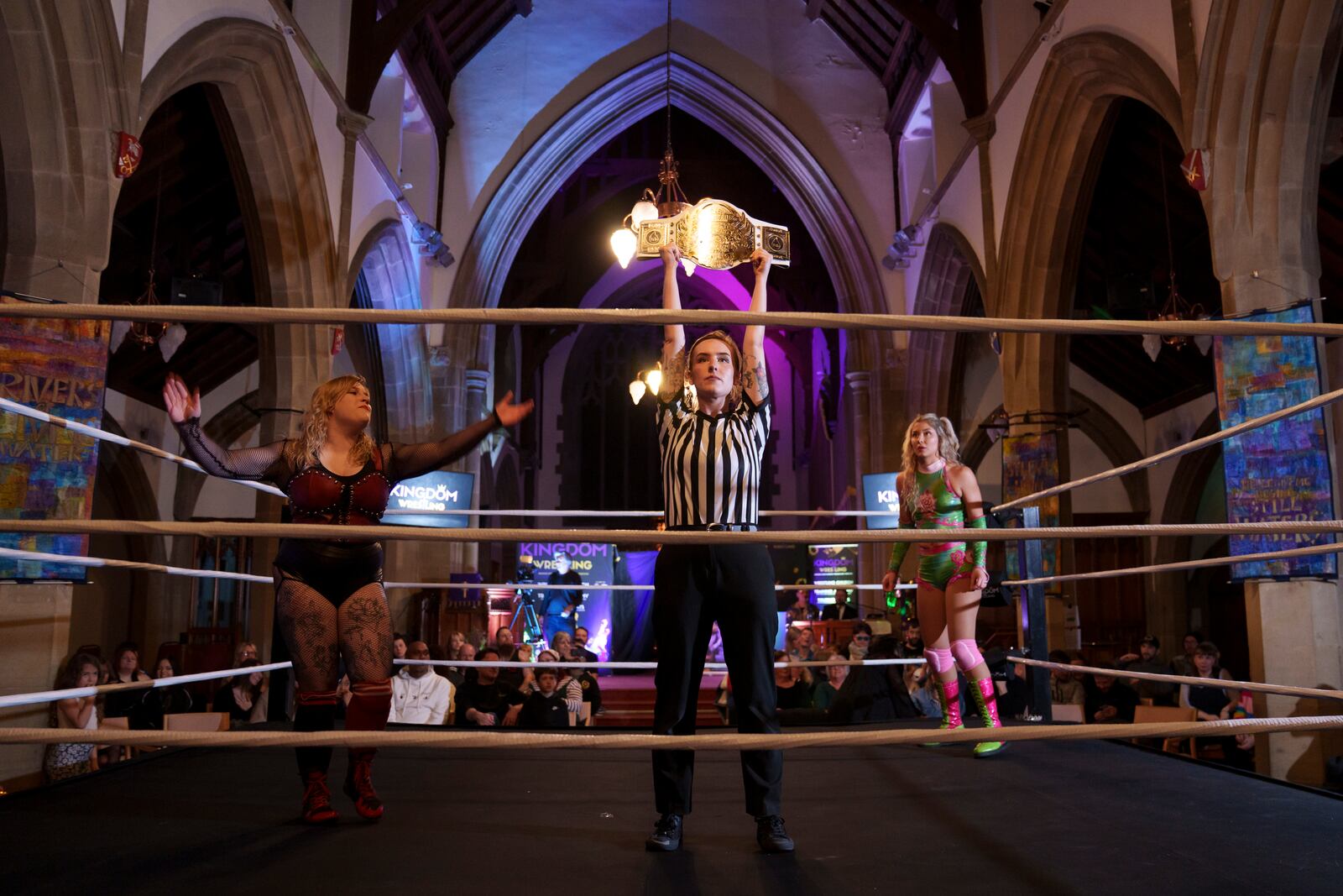 Referee Katie Crosby holds up the contested belt before Tiara's bout against Sarlett, left, during a Kingdom Wrestling show at St Peter's Church in Shipley, Saturday, March 29, 2025. (AP Photo/Jon Super)
