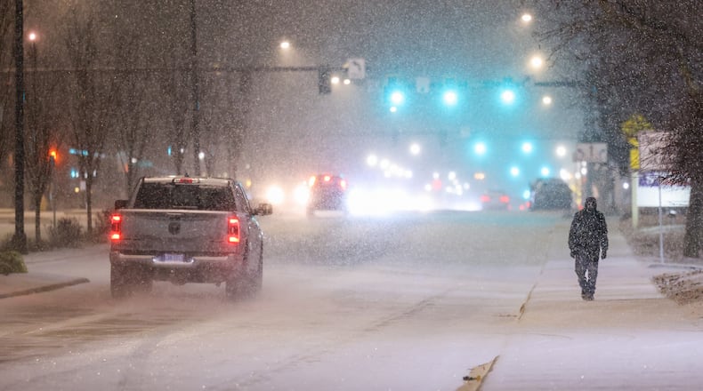 A man (right) walks as vehicles drive on West Main Street in Troy on Saturday, Jan. 24, 026. By 10 a.m. Sunday, the Miami Valley region was experiencing around 12 inches of snow in some areas. Visit DaytonDailyNews.com for the latest snow coverage. BRYANT BILLING/STAFFRYANT BILLING/STAFF