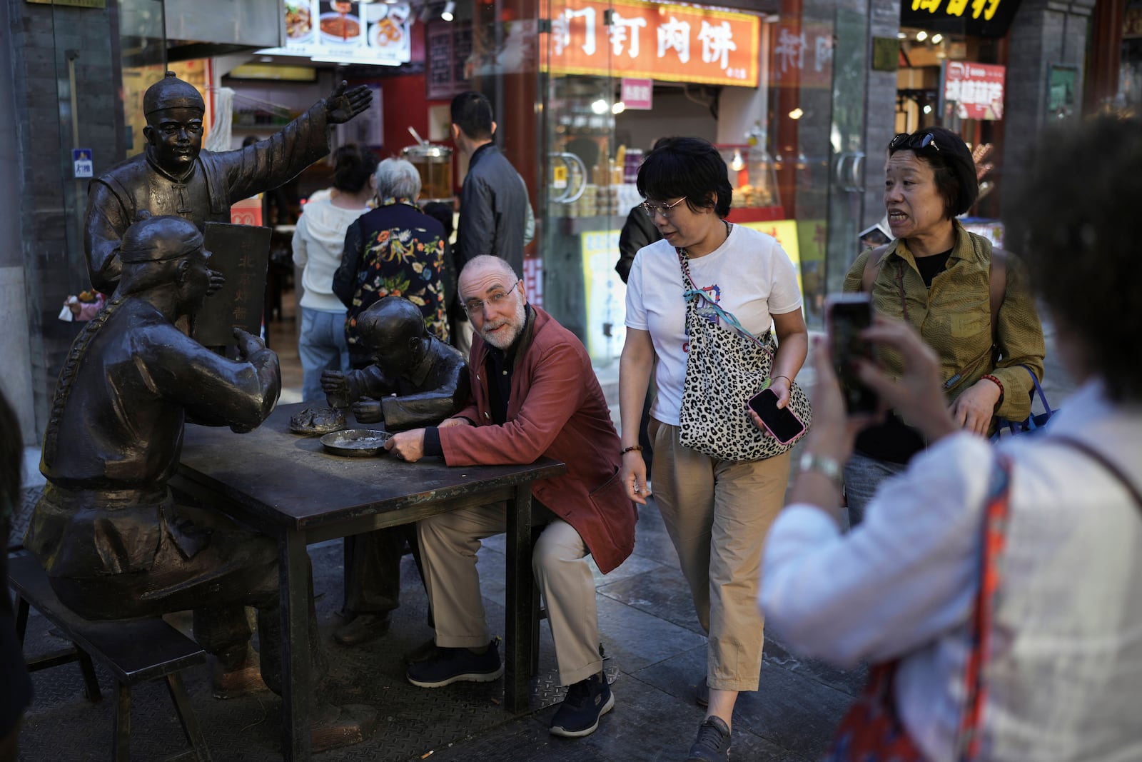 Women walk by a tourist posing for a photo with statues on display at Qianmen pedestrian shopping street in Beijing, Sunday, April 27, 2025. (AP Photo/Andy Wong)