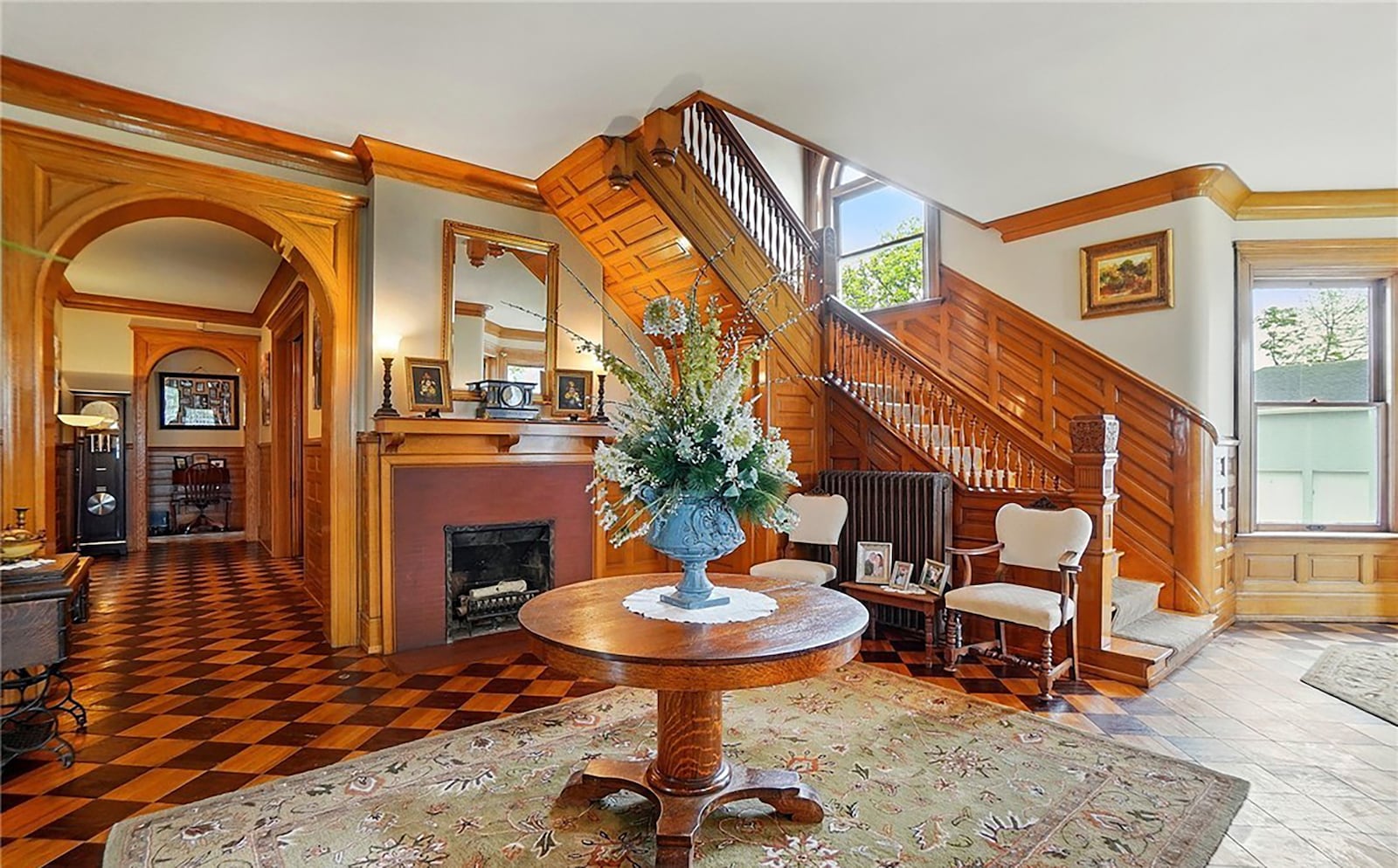 The grand foyer has parquet wood floors, a decorative fireplace and original wood details like crown molding and a carved staircase.
