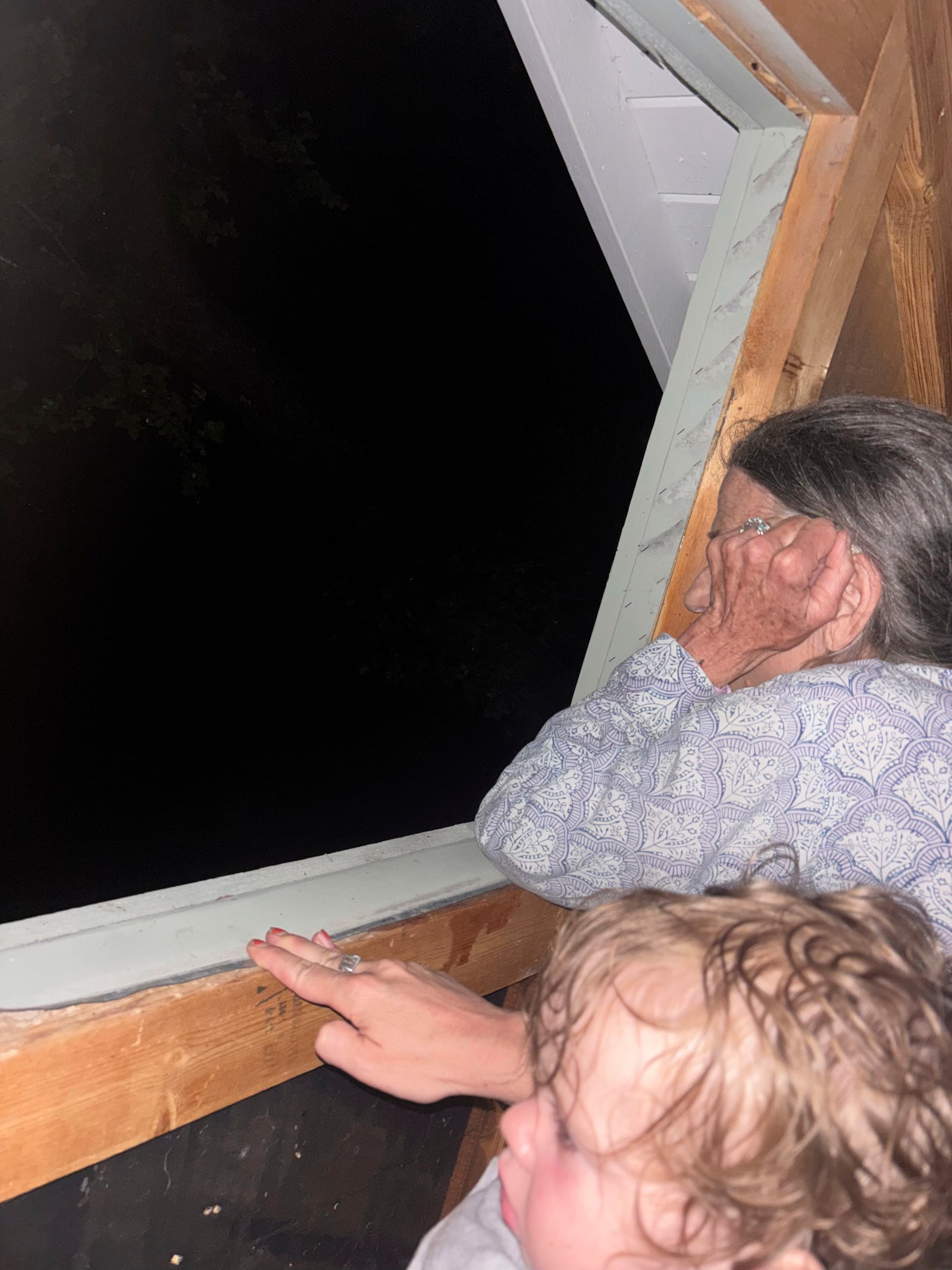 Shabd Simon-Alexander's one-year-old daughter and Jane Towler, sit in the attic of the roof of her son's cabin to escape floodwaters from the Guadalupe River in Hunt, Texas, at 6:05 a.m. on Friday, July 4, 2025. (Shabd Simon-Alexander via AP)
