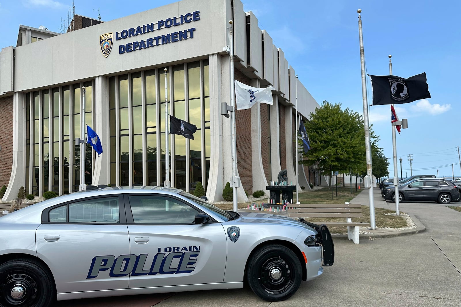 Candles sit on a memorial and flags fly at half-staff outside the police department in Lorain, Ohio, on Thursday, July 24, 2025, a day after three officers were wounded in a shooting ambush. (AP Photo/John Seewer)