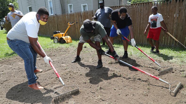 Volunteers from the 1159 South Community Development Corporation including Dorian Hunter and Te'Vaun Stephens work on a new community space at the intersection of South Yellow Springs Street and Innisfallen Avenue Friday. BILL LACKEY/STAFF