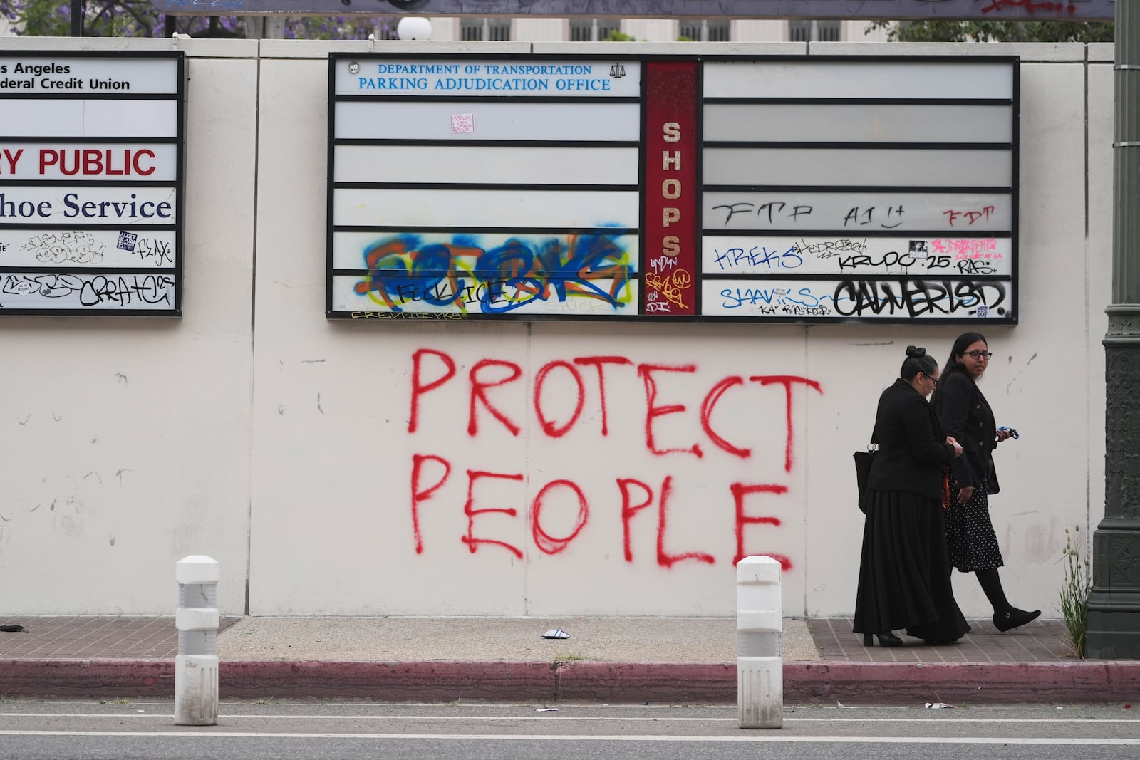 People walk past graffiti from recent protests against federal immigration raids, Wednesday, June 11, 2025, in Los Angeles. (AP Photo/Damian Dovarganes)