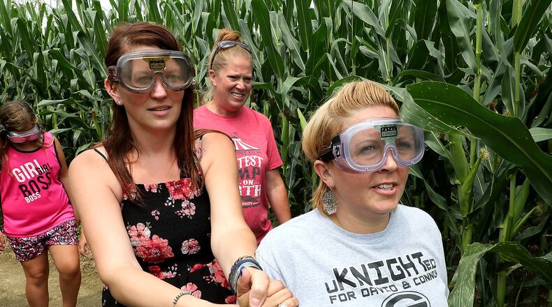 Sunnie Jenkins, left, and Aryn Waag, right hold hands as they try to navigate the corn maze at Youngs Jersey Dairy with impaired driving goggles on Tuesday. The demonstration was part of the Drive Sober or Get Pulled Over Kick-Off at Young’s. BILL LACKEY/STAFF