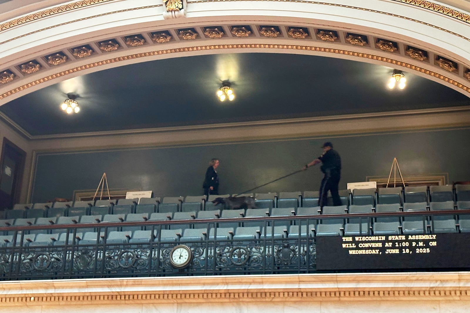 A police officer with a bomb-sniffing dog scans the public viewing gallery inside the Wisconsin state Assembly chamber, a sign of increased security following the killing of a lawmaker in neighboring Minnesota on Wednesday, June 18, 2025, in Madison, Wis. (AP Photo/Scott Bauer)