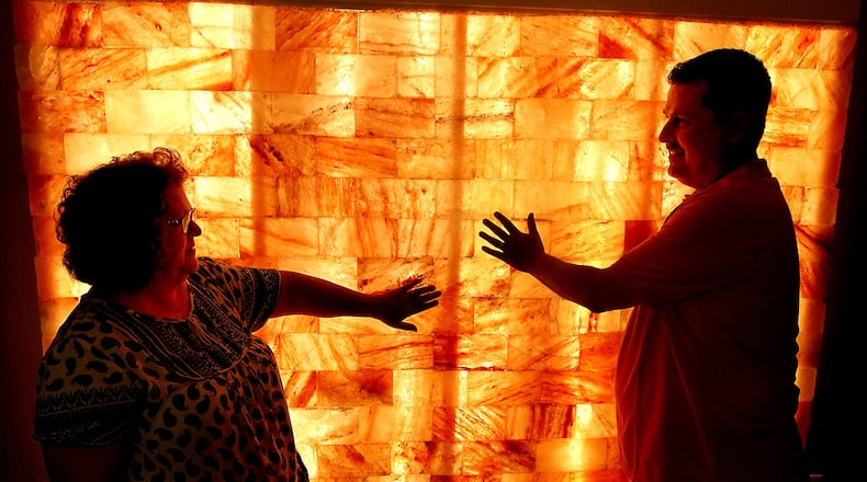 Brad or Sharon Wallace, owners of the NaCl Salt Spa in Urbana, touch the glowing wall made of Himalayan salt in one of the theropy rooms Tuesday, June 20, 2017. Bill Lackey/Staff