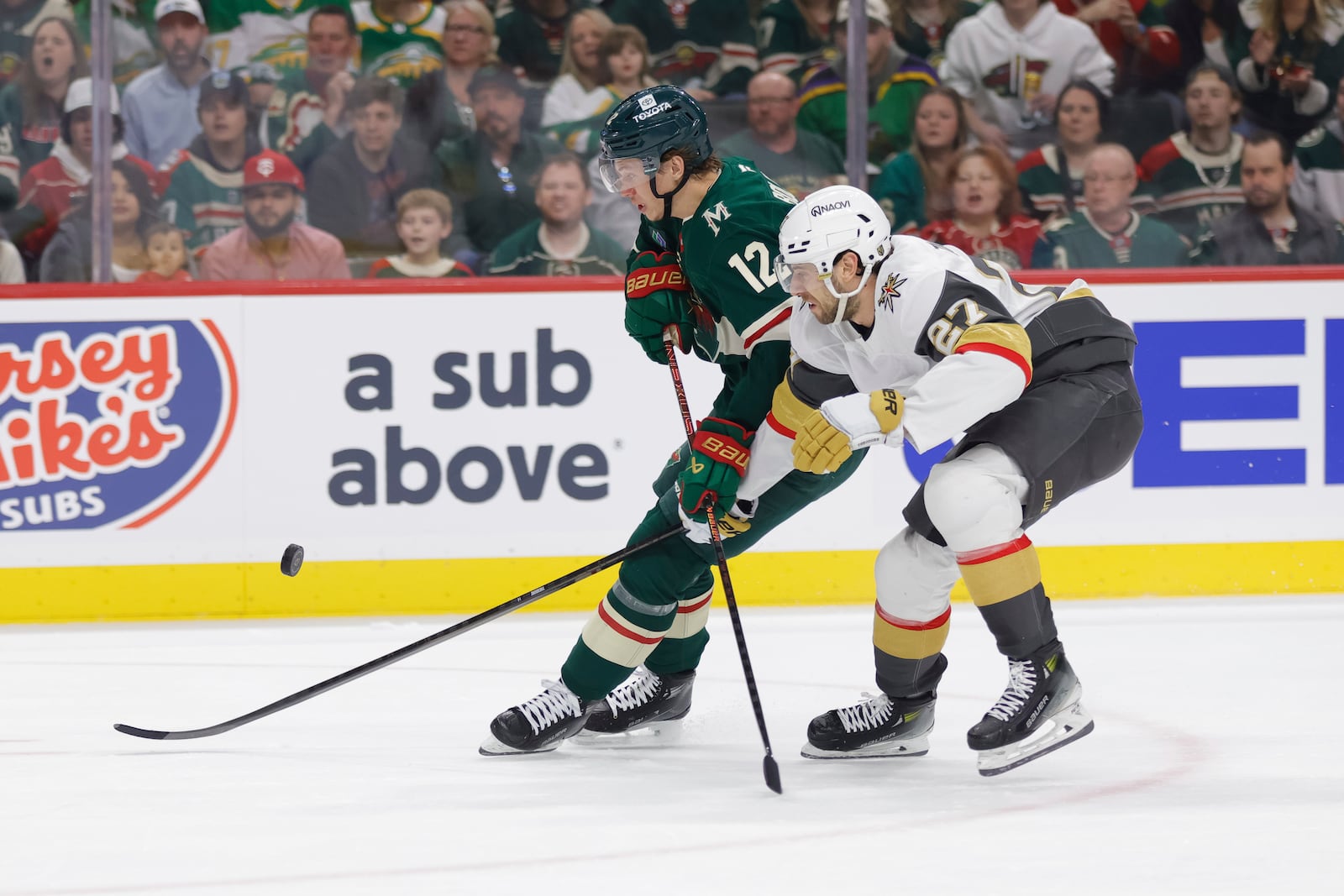Minnesota Wild left wing Matt Boldy (12) and Vegas Golden Knights defenseman Shea Theodore (27) battle for the puck during the first period of Game 6 of a first-round NHL hockey playoff series Thursday, May 1, 2025, in St. Paul, Minn. (AP Photo/Bailey Hillesheim)