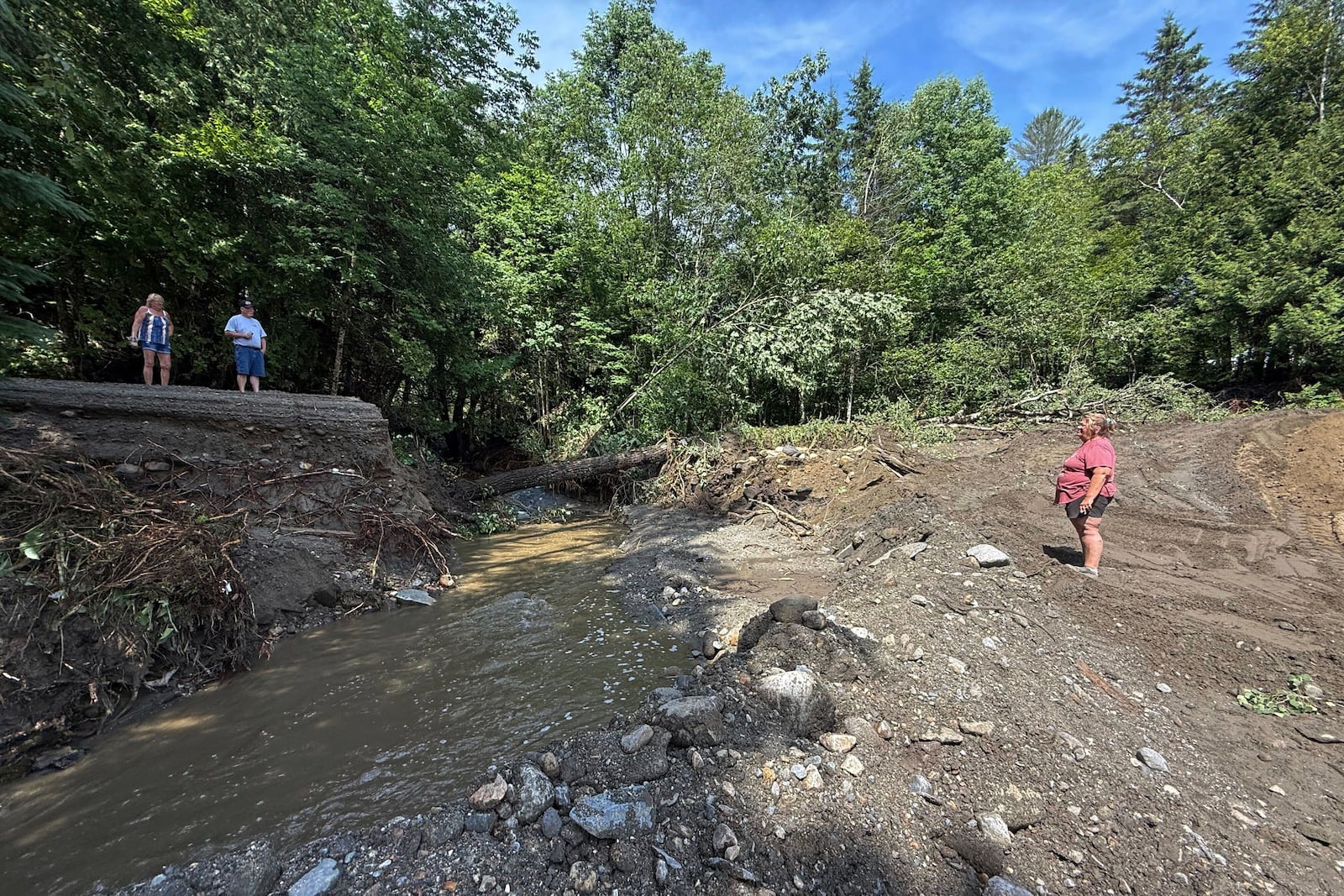 Michelle Tanner, whose yard was washed away by flash flooding, stands in what used to be her driveway as she talks with neighbors on a destroyed roadway, Friday, July 11, 2025 in Sutton, Vt. (AP Photo/Amanda Swinhart)