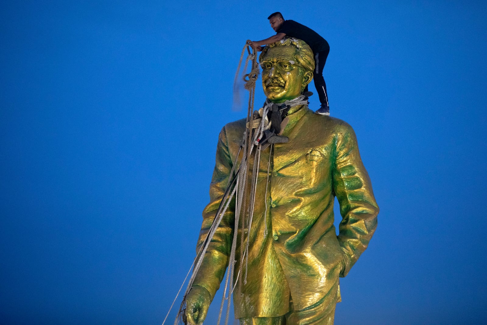 FILE - A man climbs to tie a rope around the head of a large statue of Sheikh Mujibur Rahman, father of Bangladesh leader Sheikh Hasina, as protesters try to bring it down after she resigned as Prime Minister, in Dhaka, Bangladesh, on Aug. 5, 2024. (AP Photo/Rajib Dhar, File)
