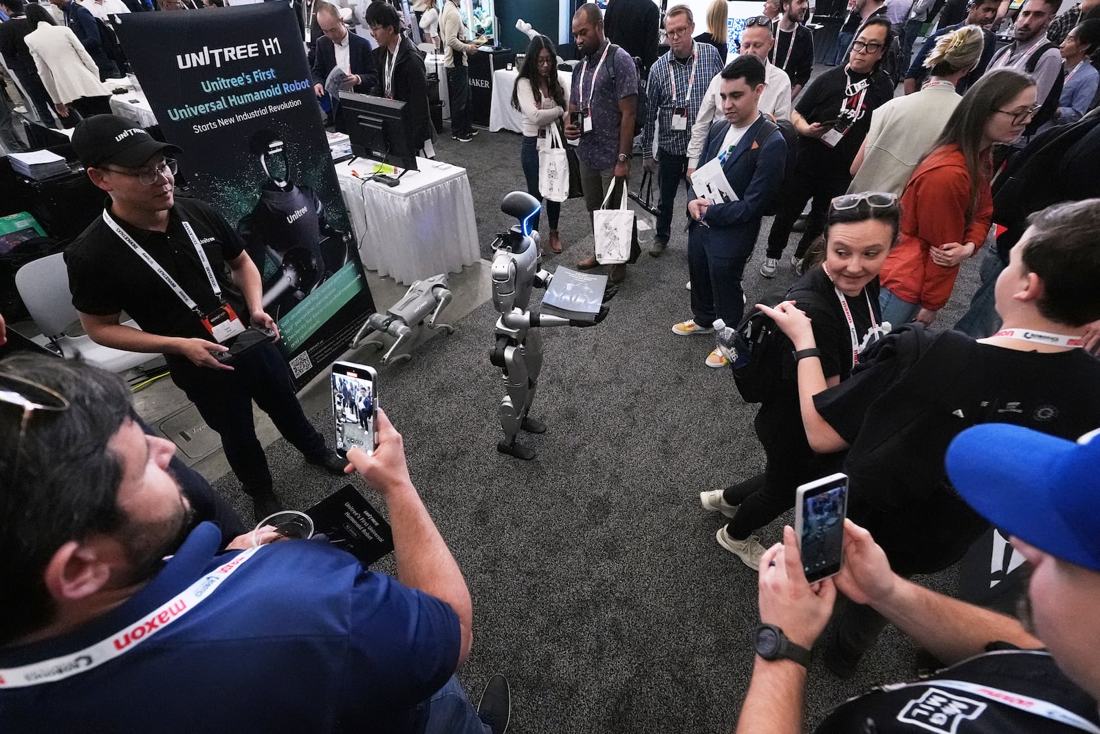 A human-like Unitree robot is surrounded by convention guests while passing out company brochures at the Robotics Summit & Expo, Wednesday, April 30, 2025, in Boston. (AP Photo/Charles Krupa)