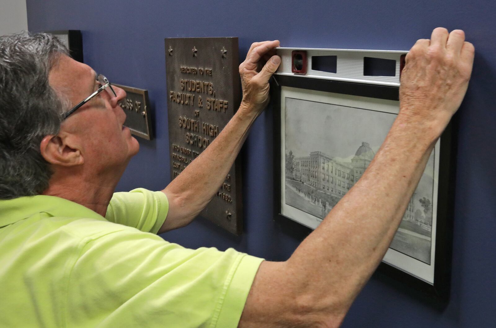 Don McKanna, one of the owners of Frame Haven, hangs old pictures and plaques from Springfield City School's past in the lobby of John Legend Theater Friday. BILL LACKEY/STAFF