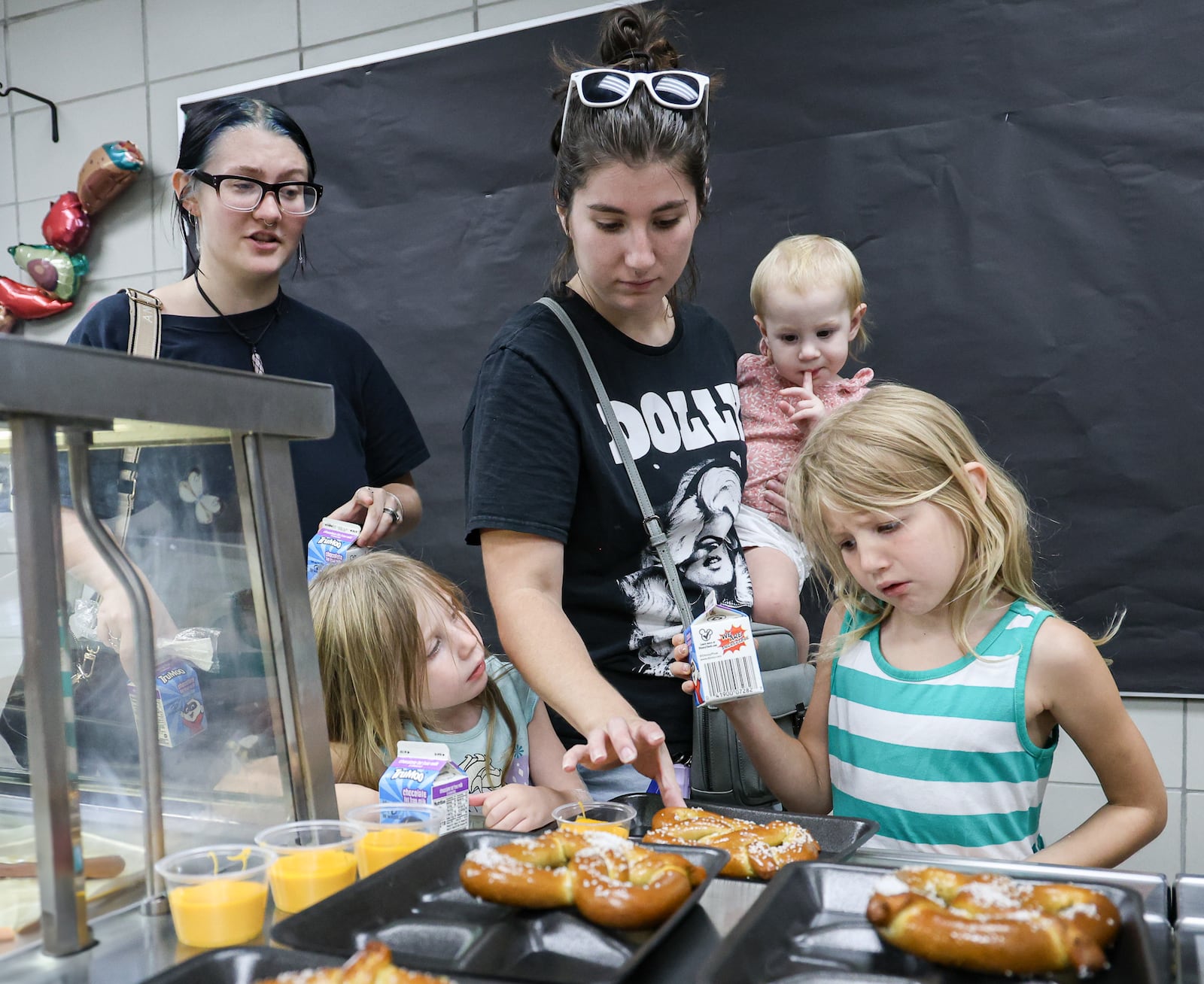 Dana, the mother of Emmy (bottom left), Violet (top center) and Ava (bottom right), grabs a pretzel for her children as her sister Abby watches during a summer lunch program organized by Kettering City Schools on Friday, Aug. 1 at Greenmont Elementary School. Friday was the final day for the program, which started June 2. BRYANT BILLING / STAFF
