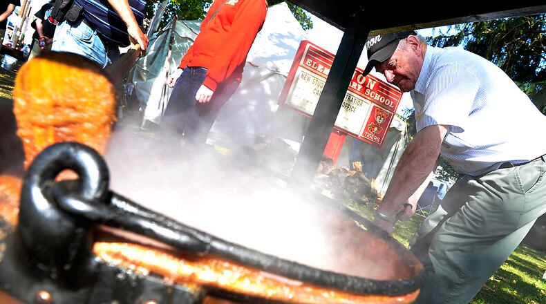 Warren Lyon places a fresh log on the fire burning under a bubbling cauldron of apple butter as he stokes the fire to keep the butter cooking during the Enon Apple Butter Festival. Bill Lackey/Staff