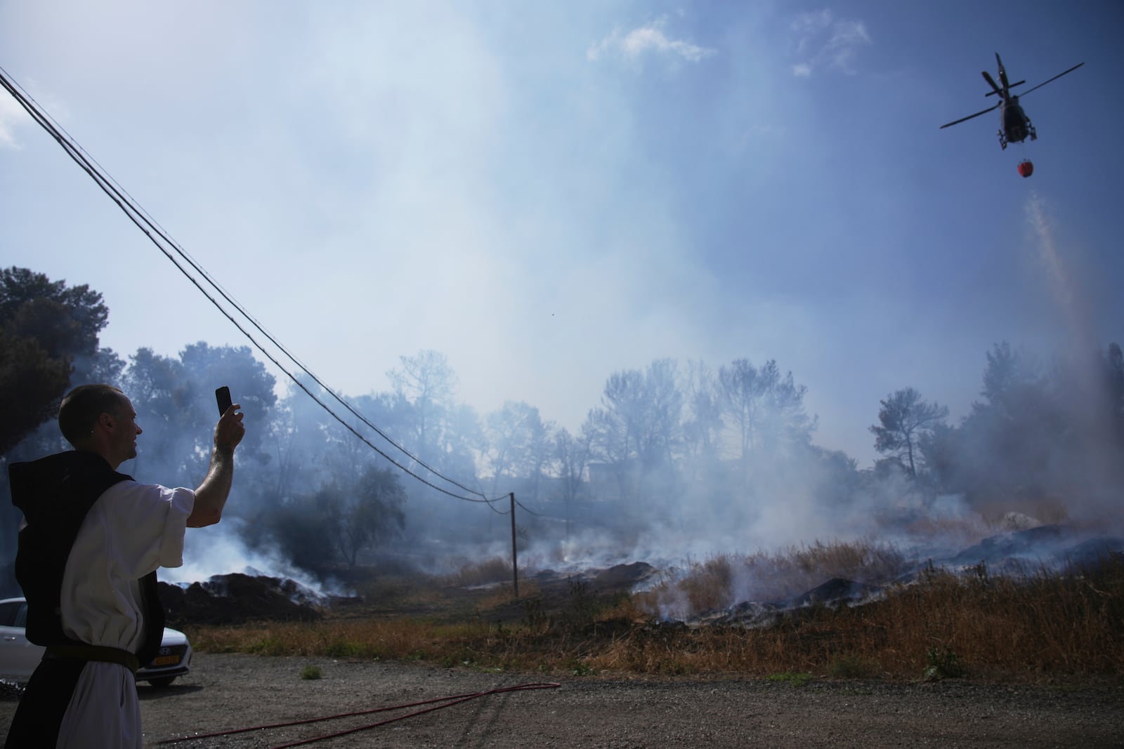 A Roman Catholic Trappist monk films an Israeli fire crew helicopter battling a wildfire outside his monastery in Latrun, Israel, outside of Jerusalem, Thursday, May 1, 2025. (AP Photo/Ohad Zwigenberg)