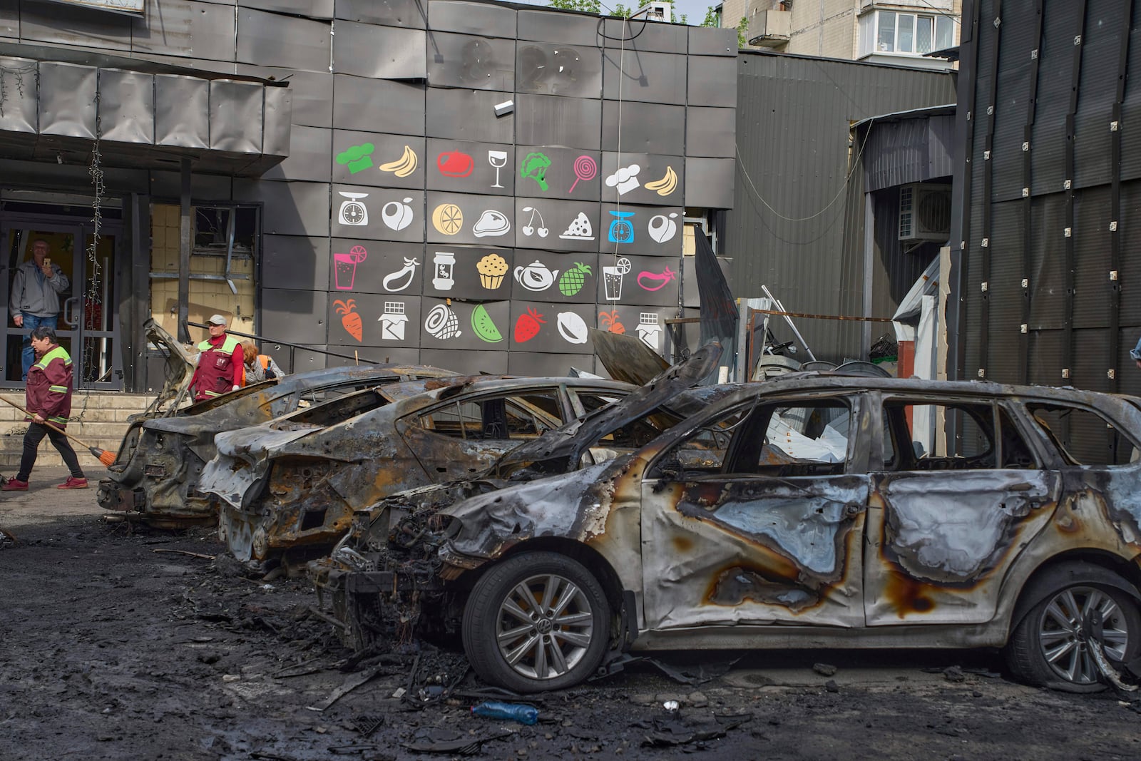 Municipal workers clean up near burnt cars in the residential area following Russia's drone attack in Kyiv, Ukraine, Sunday, May 4, 2025. (AP Photo/Efrem Lukatsky)
