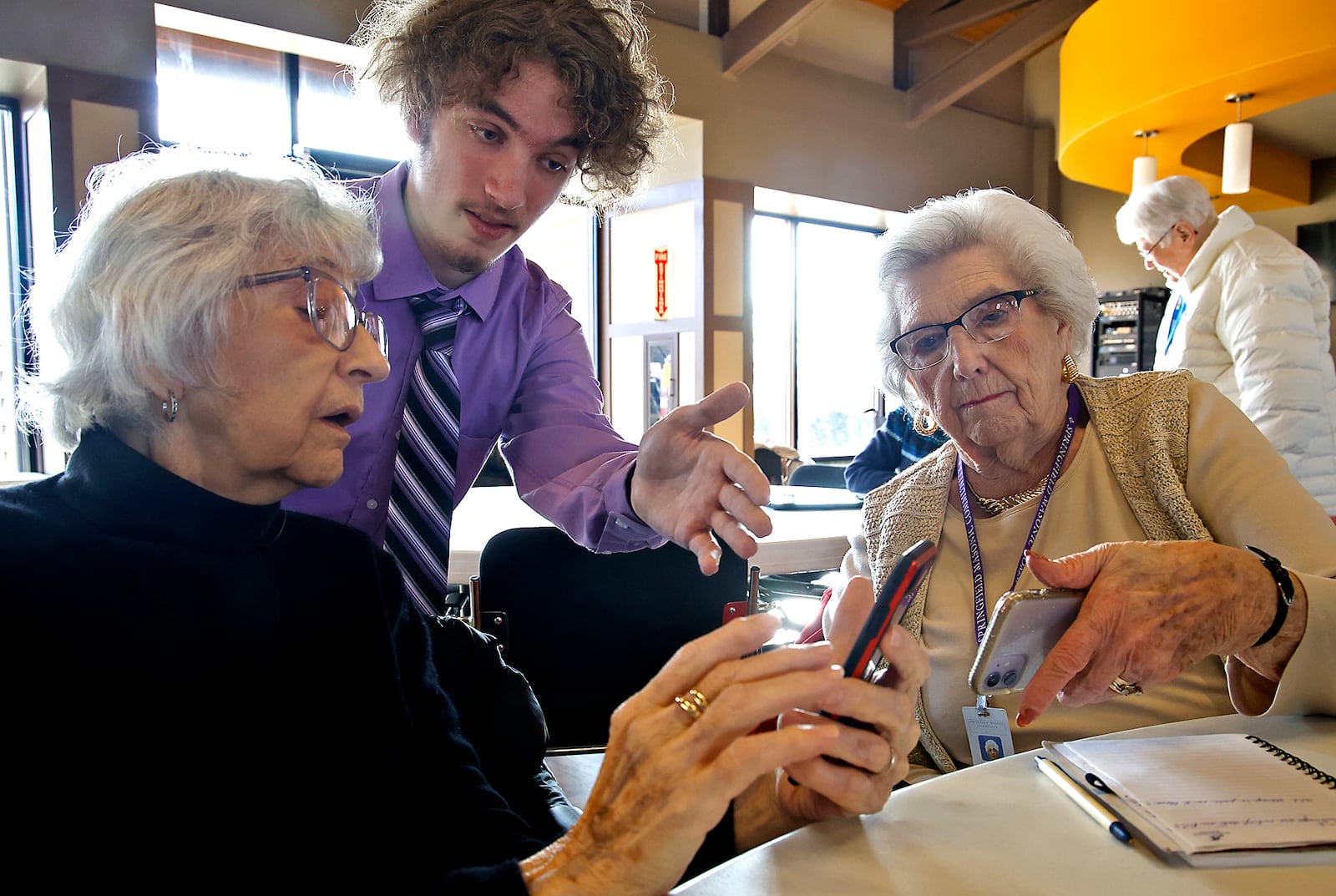 Clayton Shumway, from the Springfield/Clark CTC, helps Carol Warren, left, and Dorothy Neer, both residents of the Springfield Masonic Community, with her phone Friday, Feb. 23, 2024. Sabastian and several other Cyber Security students from CTC were at the Masonic Community to help the seniors with technology. BILL LACKEY/STAFF