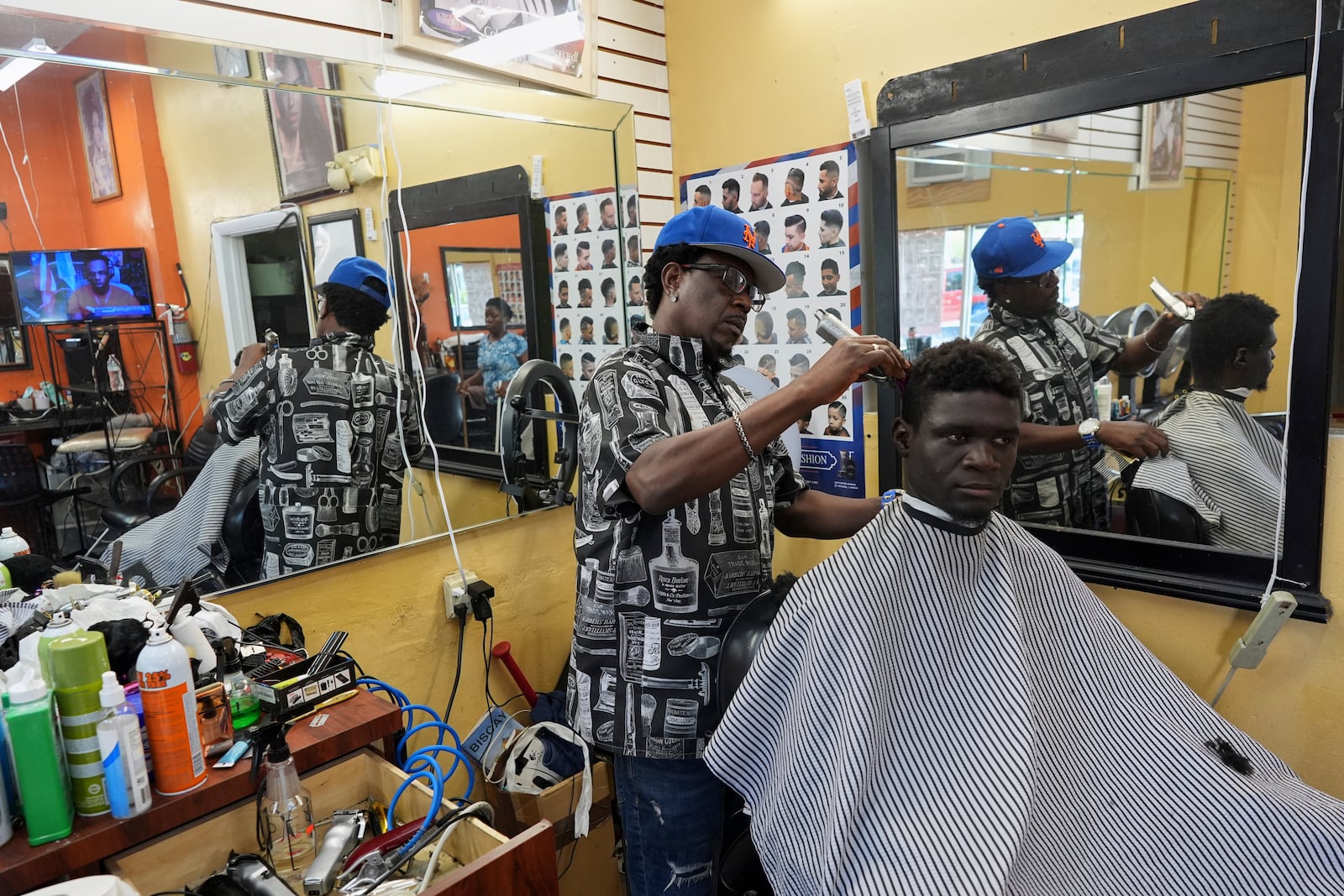 FILE - Creole-language news airs on a TV as barber Charlemagne Merilien cuts a client's hair inside Els Beauty Salon in Miami's Little Haiti neighborhood, June 6, 2025. (AP Photo/Rebecca Blackwell, File)