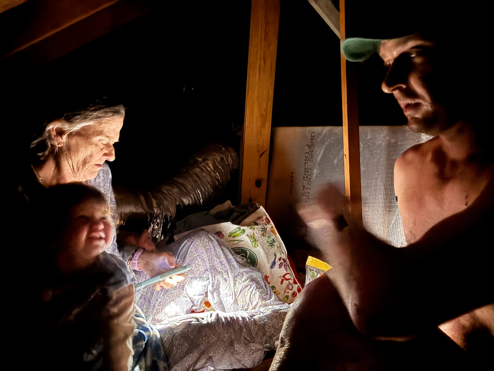 From left, Jane Towler, Shabd Simon-Alexander's one-year-old daughter, Alden Towler, and Simon-Alexander, not pictured, sit in the attic of his cabin to escape floodwaters from the Guadalupe River in Hunt, Texas, at 4:27 a.m. on Friday, July 4, 2025. (Shabd Simon-Alexander via AP)