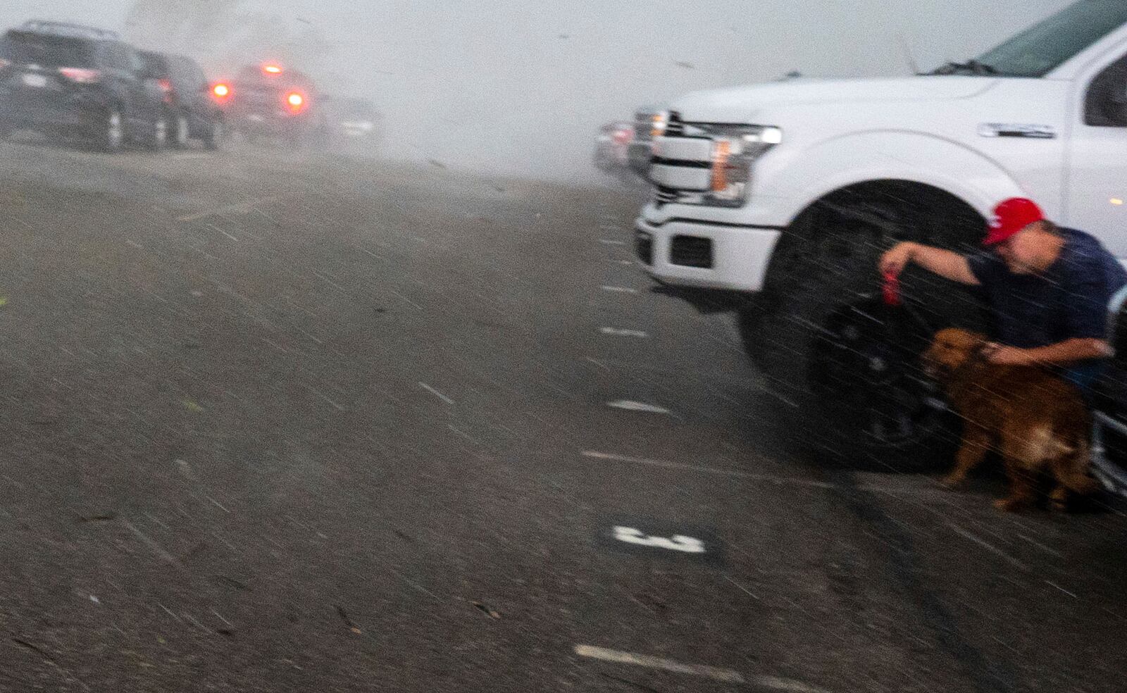 A man and his dog duck behind a truck as the storm hits at Fort Cherry High School in McDonald, Pa., Tuesday, April 29, 2025. (Lucy Schaly/Pittsburgh Post-Gazette via AP)