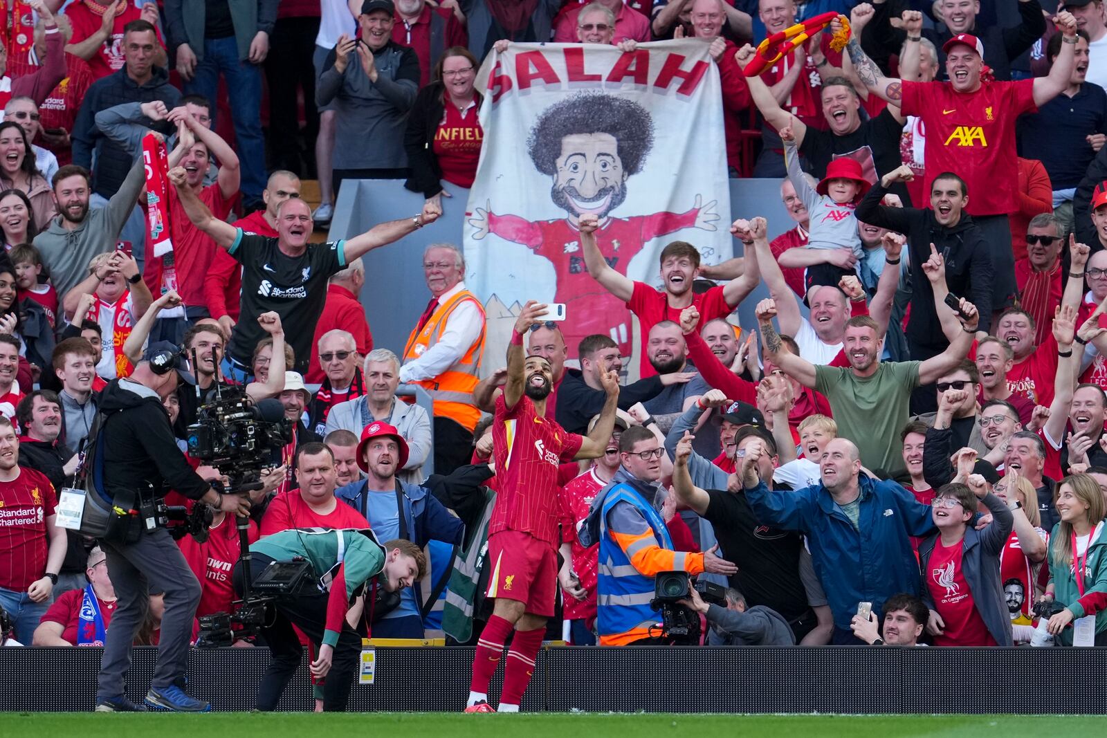 Liverpool's Mohamed Salah takes a selfie with a fans smartphone as he celebrates after scoring his side's fourth goal during the English Premier League soccer match between Liverpool and Tottenham Hotspur at Anfield in Liverpool, England, Sunday, April 27, 2025. (AP Photo/Jon Super)