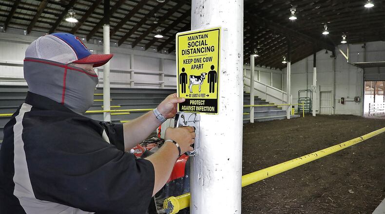 Brad Spencer hangs signs in the barns at the Clark County Fairgrounds Thursday reminding fairgoers to social distance. BILL LACKEY/STAFF