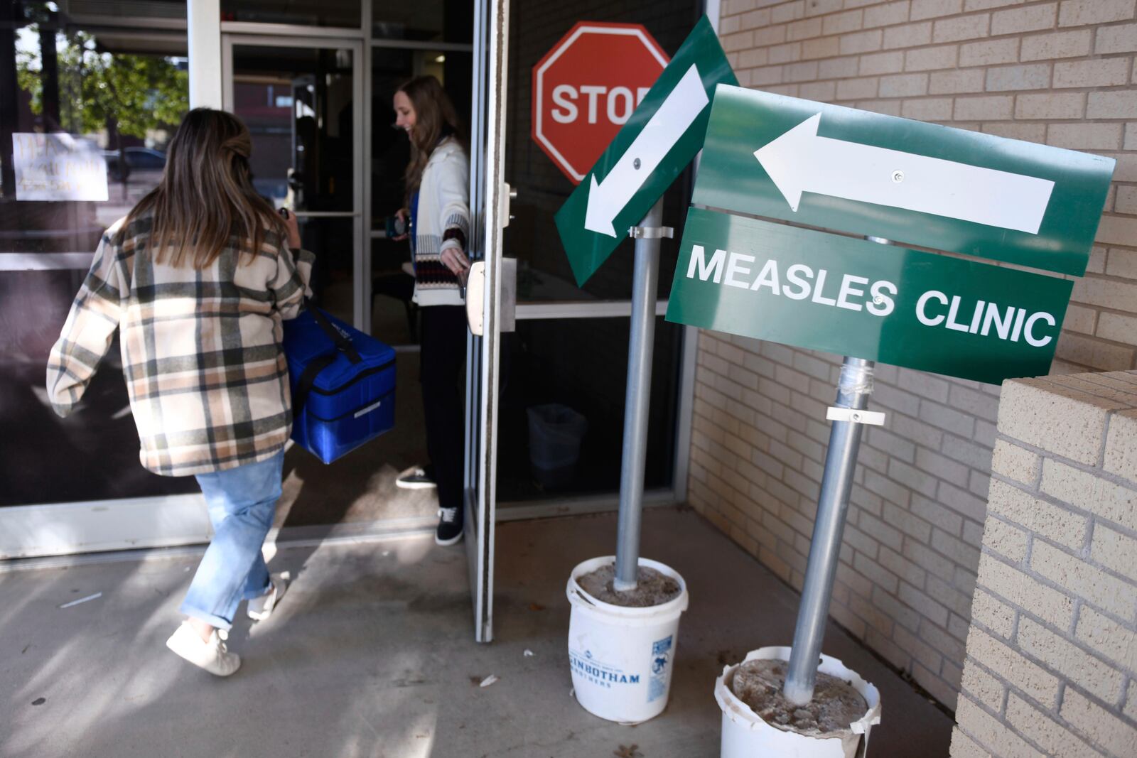 Health department staff members enter the Andrews County Health Department measles clinic carrying doses of the measles, mumps and rubella vaccine, Tuesday, April 8, 2025, in Andrews, Texas. (AP Photo/Annie Rice)