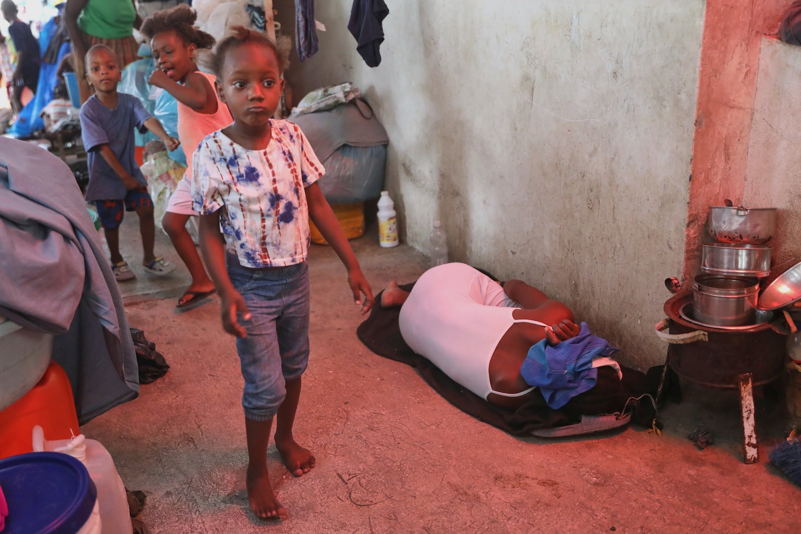 A woman sleeps on a blanket next to children playing in a hallway at a shelter for families displaced by gang violence in Port-au-Prince, Haiti, Monday, May 12, 2025. (AP Photo/Odelyn Joseph)