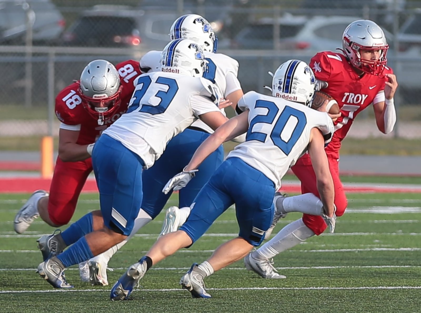 Troy's Aiden Kirkpatrick (7) looks for an opening as teammate Landen Adkins (18) blocks while Xenia's Cecil Piner (33) and Tyler Thompson (20) pursue during their game Friday, Aug. 29, 2025, at Troy Memorial Stadium. Troy won 24-14. Steve Black / Staff
