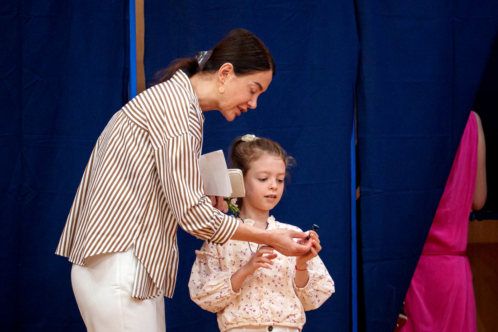 A woman hands a little girl a voting stamp after exiting a voting booth before casting her vote in the first round of the presidential election redo in Bucharest, Romania, Sunday, May 4, 2025. (AP Photo/Andreea Alexandru)