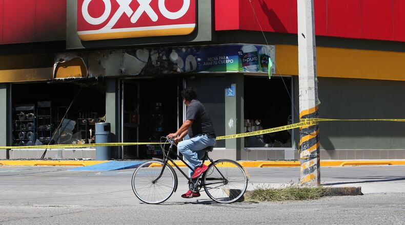 A man rides a bike next to a convenience store that was set on fire, in San Francisco del Ricon, Guanajuato state, Mexico, Sunday, Feb. 22, 2026, after the death of the leader of the Jalisco New Generation Cartel, Nemesio Ruben Oseguera Cervantes, known as "El Mencho." (AP Photo/Alfredo Valadez)